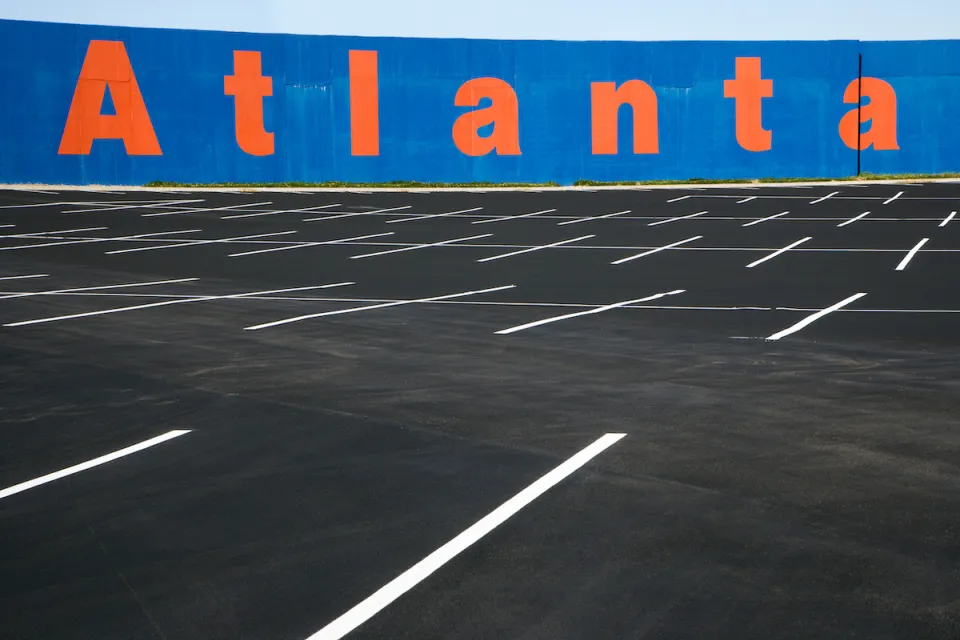 Empty asphalt parking lot with blue wall in background with Atlanta painted in orange letters.